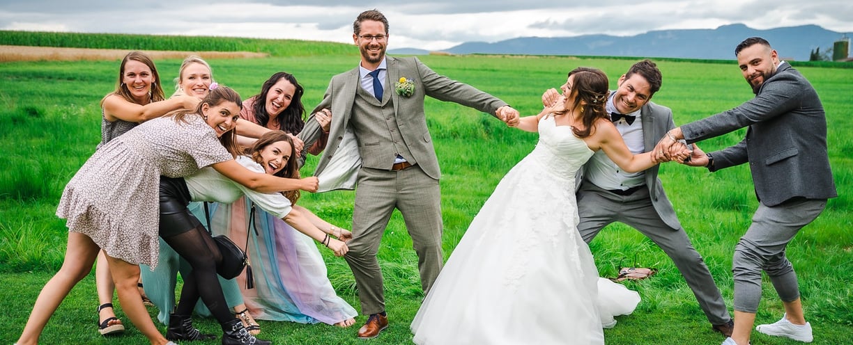 Brautpaar und Freunde beim lustigen Gruppenfoto auf der Wiese – Hochzeit von Misch & Simu