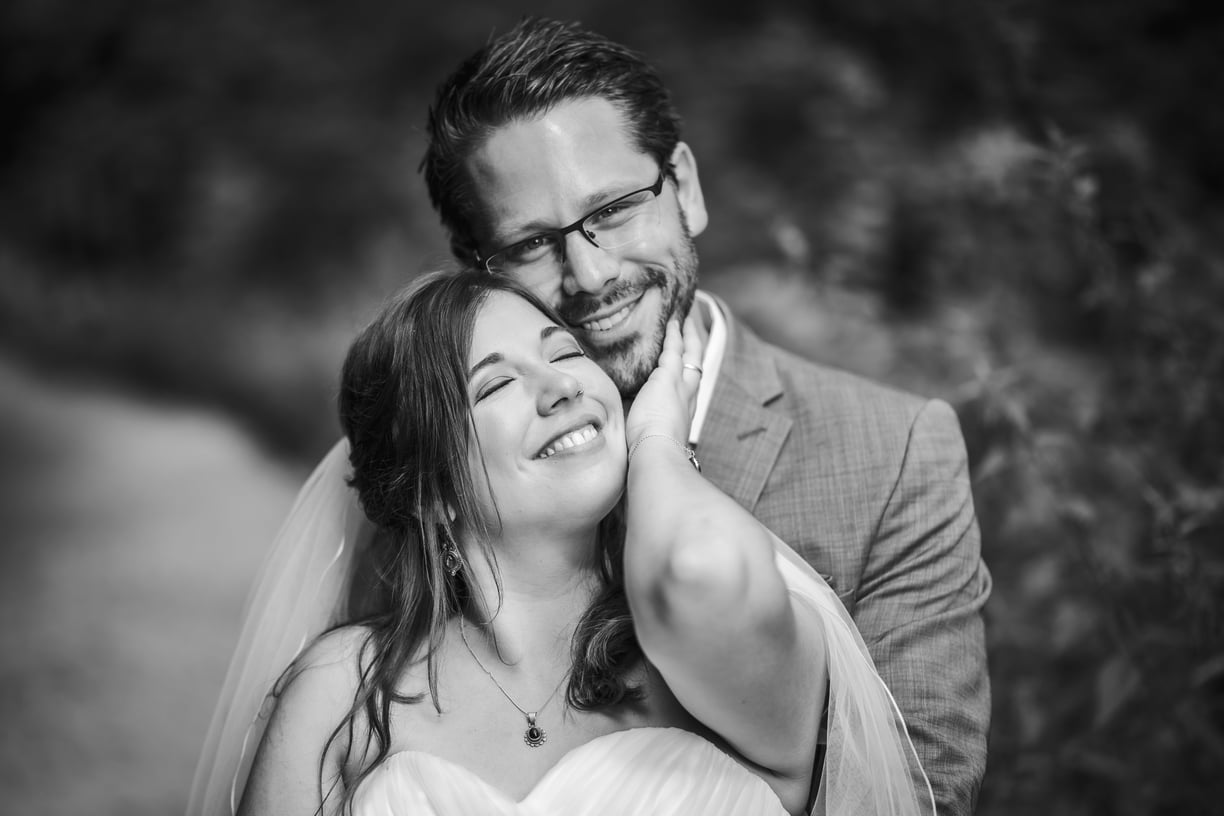 Braut schmiegt sich lachend an den Bräutigam, Schwarz-Weiss – Hochzeit von Misch & Simu