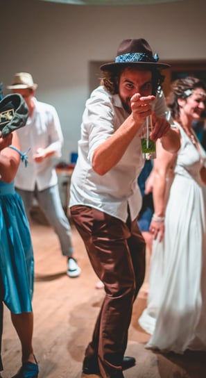 Gast mit Hut tanzt und zeigt in die Kamera – Hochzeit von Rege & Sven