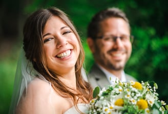 Lachende Braut, Bräutigam unscharf im Hintergrund – Hochzeit von Misch & Simu