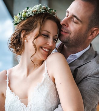 Braut mit Blumenkranz lehnt sich lächelnd an den Bräutigam – Hochzeit von Romana & Remo
