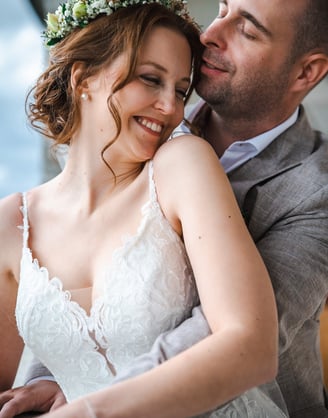 Braut mit Blumenkranz lehnt sich lächelnd an den Bräutigam – Hochzeit von Romana & Remo
