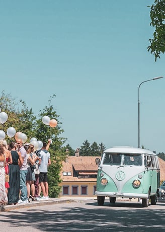 Grüner VW-Bus als Hochzeitsauto, Gäste mit Ballonen am Strassenrand – Hochzeit von Tina & Will