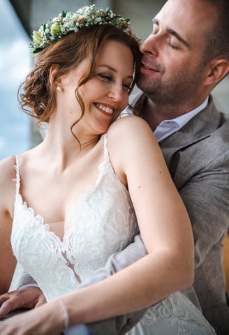 Braut mit Blumenkranz lehnt sich lächelnd an den Bräutigam – Hochzeit von Romana & Remo