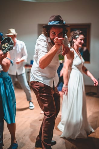 Gast mit Hut tanzt und zeigt in die Kamera – Hochzeit von Rege & Sven