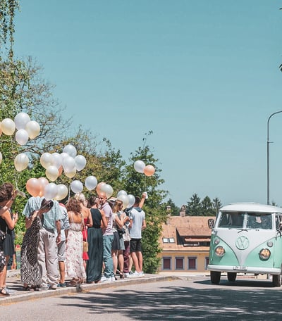 Grüner VW-Bus als Hochzeitsauto, Gäste mit Ballonen am Strassenrand – Hochzeit von Tina & Will