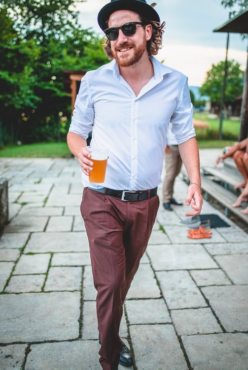Bräutigam mit Hut und Bier kommt lachend auf die Kamera zu – Hochzeit von Rege & Sven