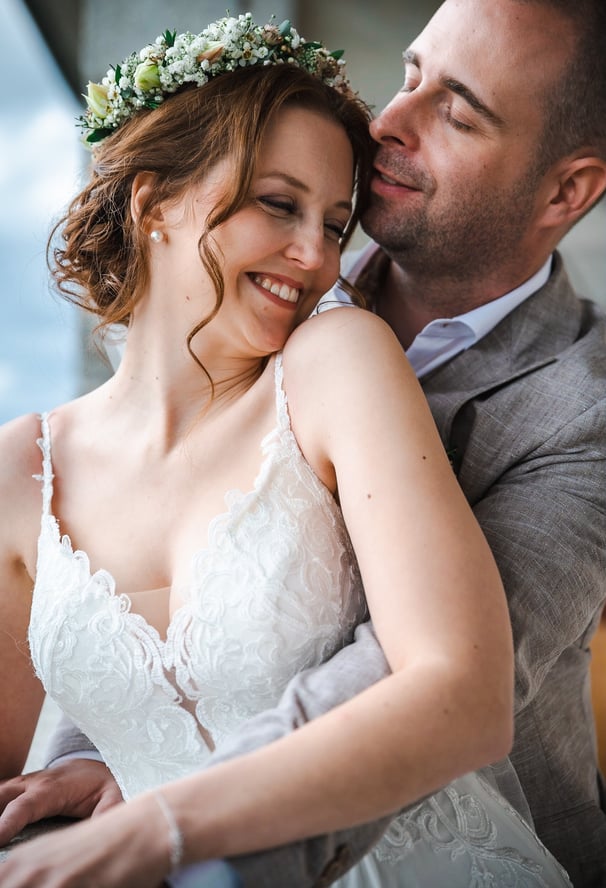 Braut mit Blumenkranz lehnt sich lächelnd an den Bräutigam – Hochzeit von Romana & Remo