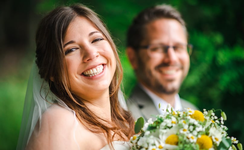 Lachende Braut, Bräutigam unscharf im Hintergrund – Hochzeit von Misch & Simu